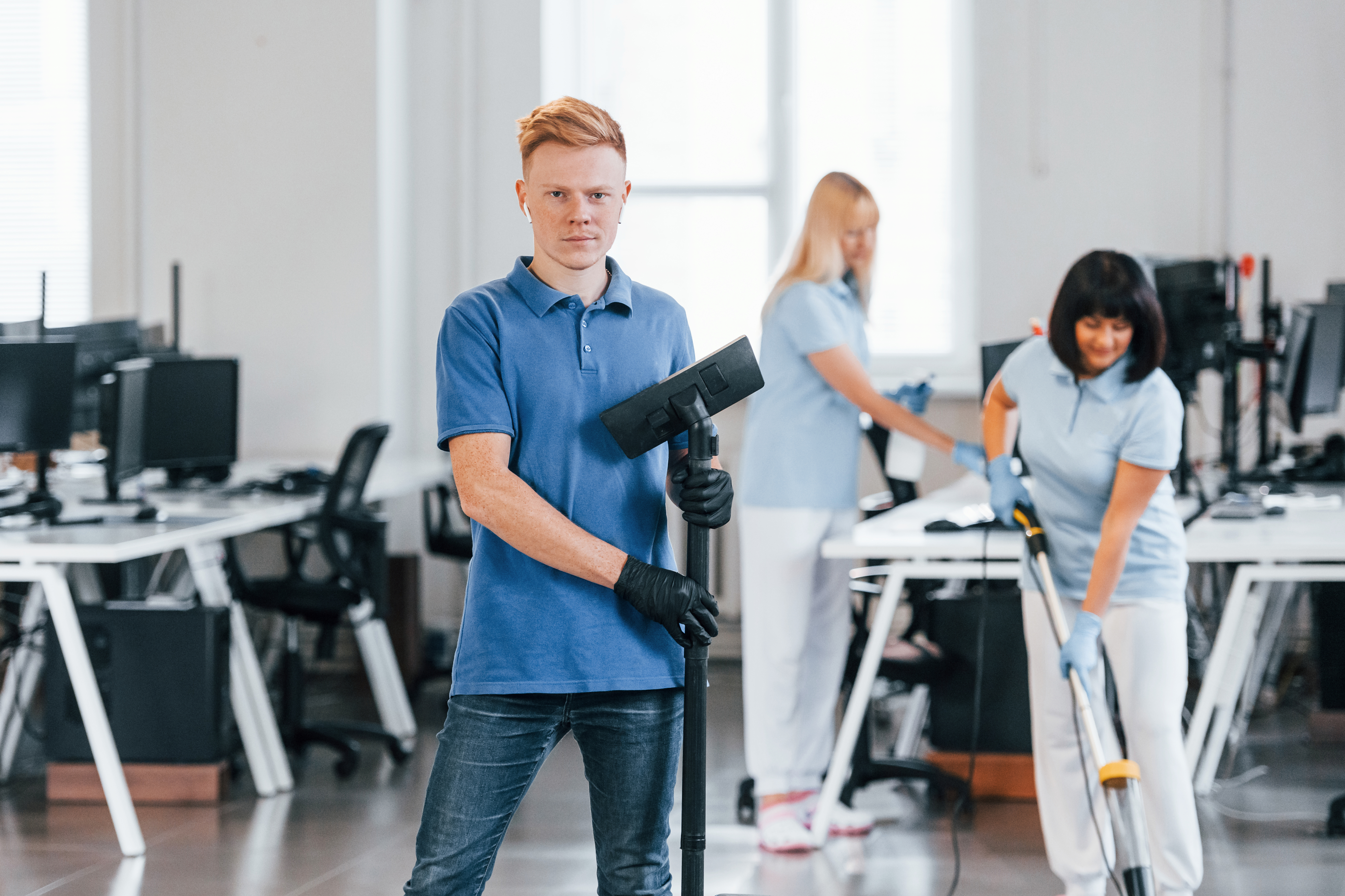 Guy with vacuum cleaner. Group of workers clean modern office together at daytime