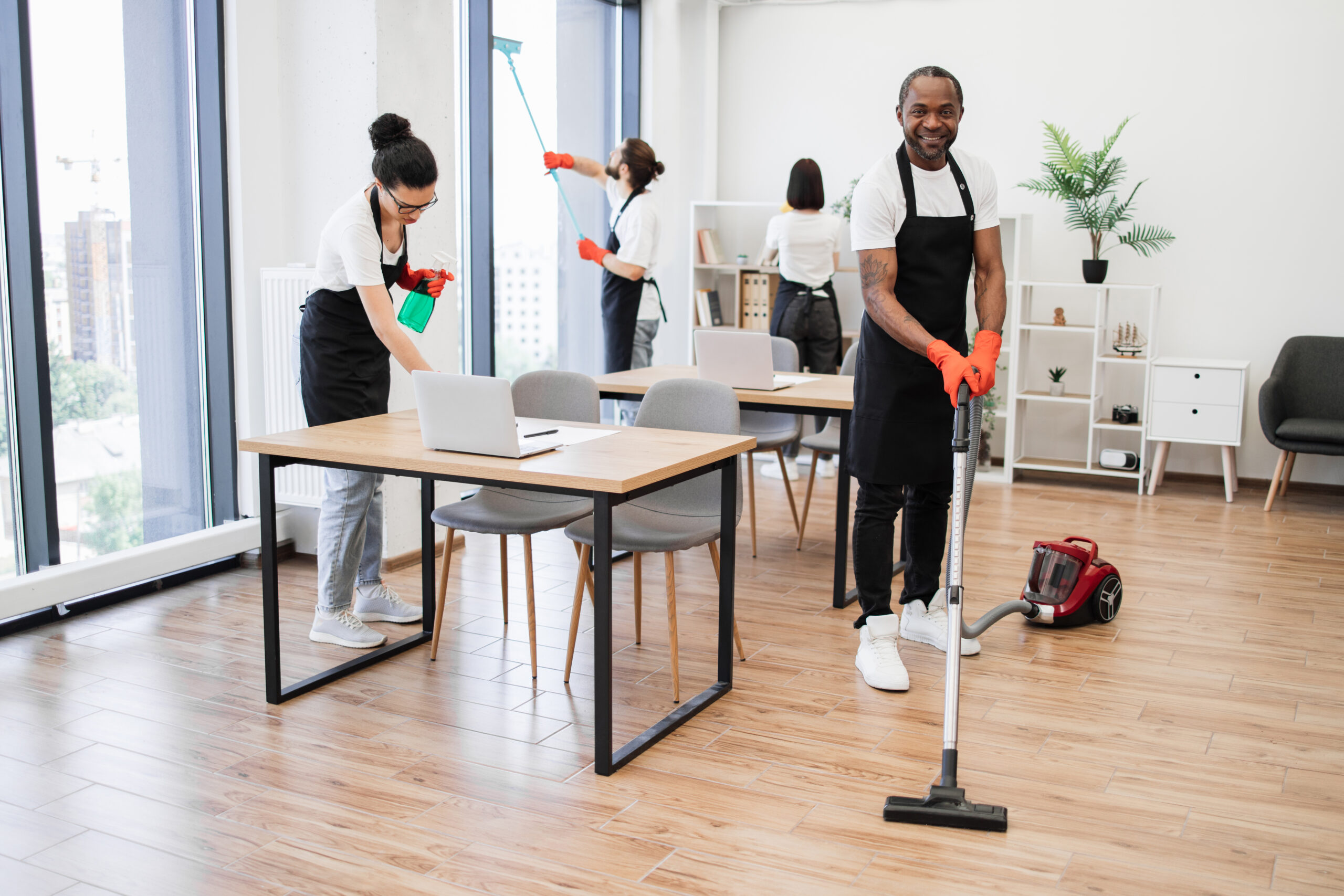African American man wearing black apron vacuuming floor of modern office.