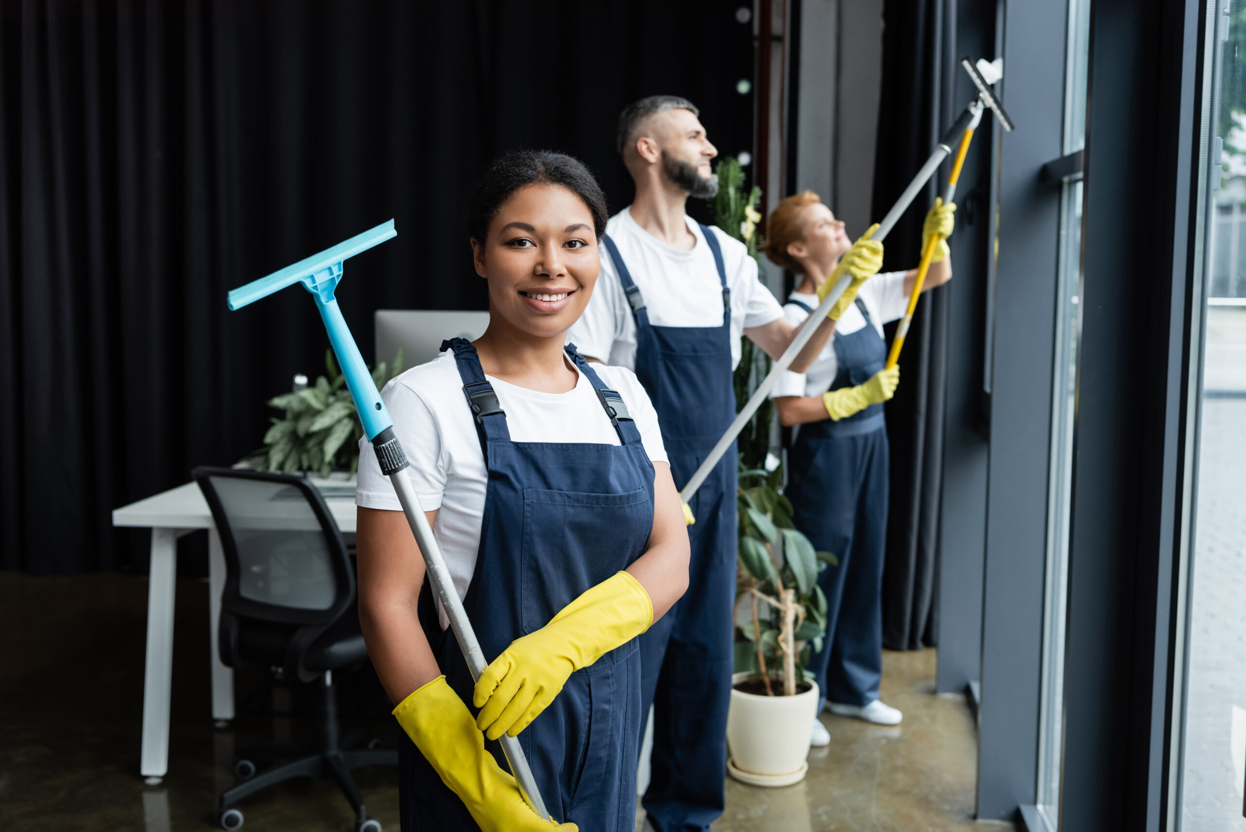 cheerful mixed race woman holding window wiper near colleagues working in office