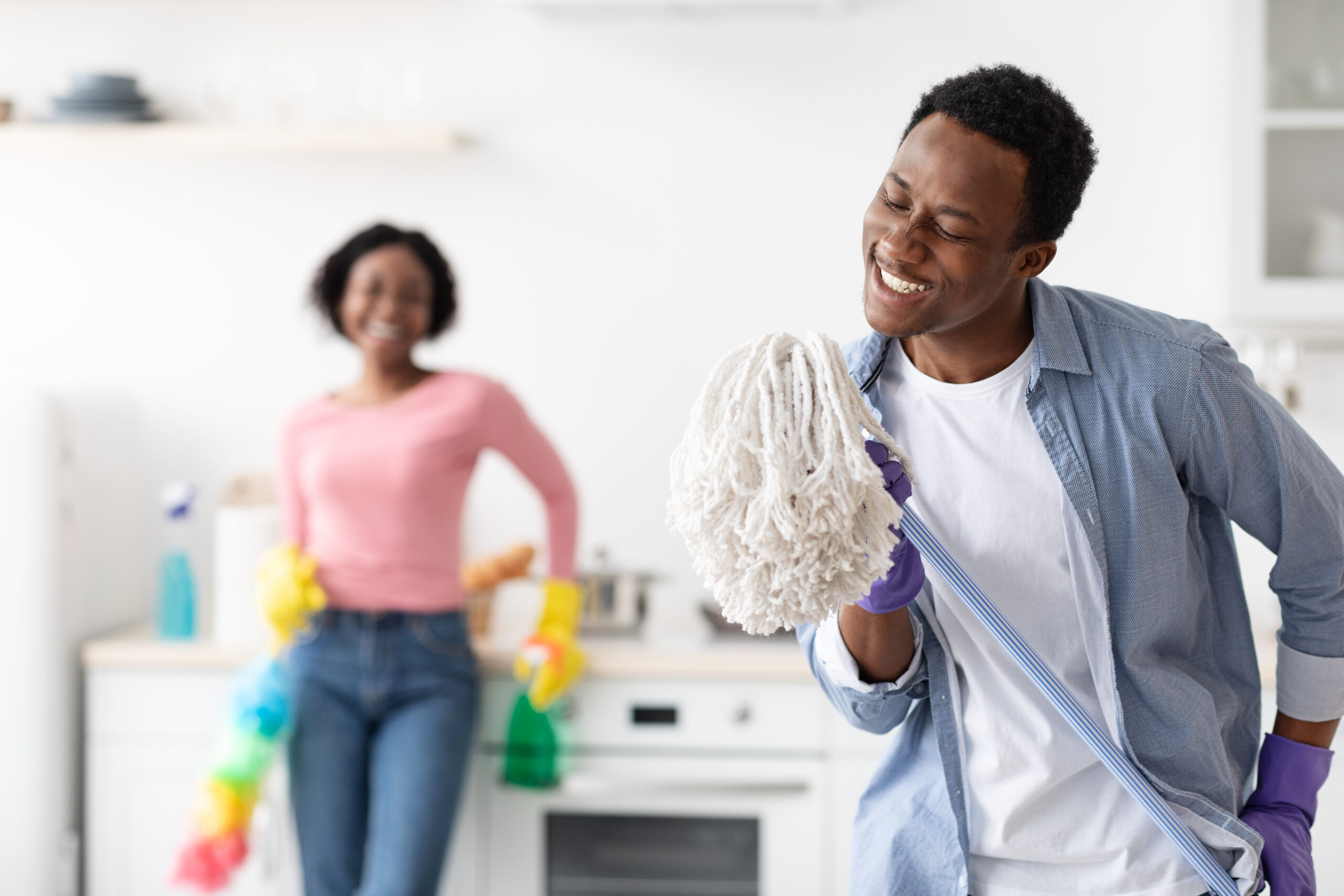Joyful black guy using mop as microphone, singing while cleaning