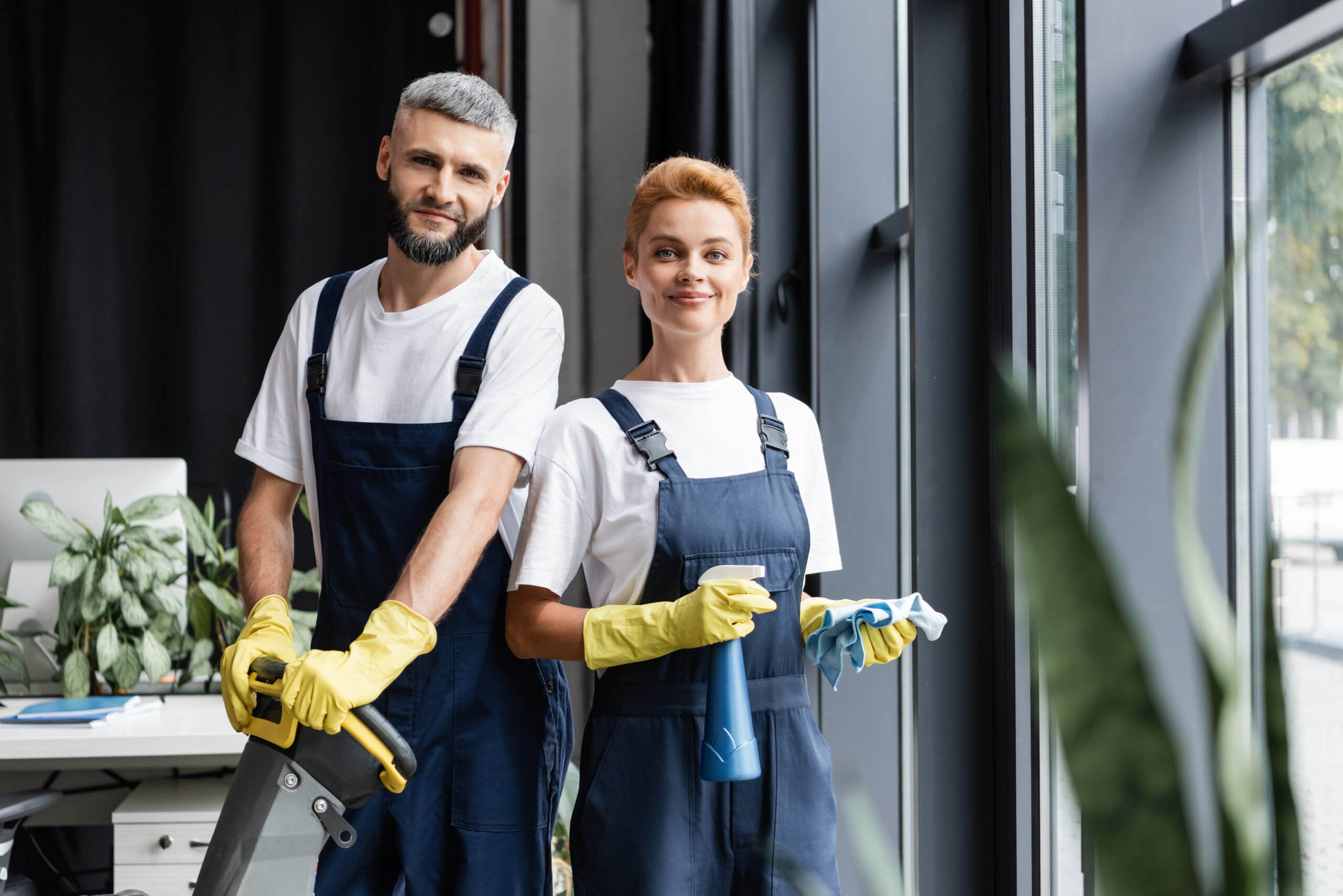 smiling professional cleaners in uniform looking at camera in office