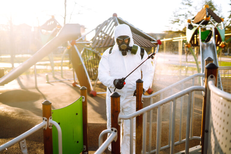 Man wearing protective suit disinfecting the playground in the sun with spray. Covid -19. Cleaning.