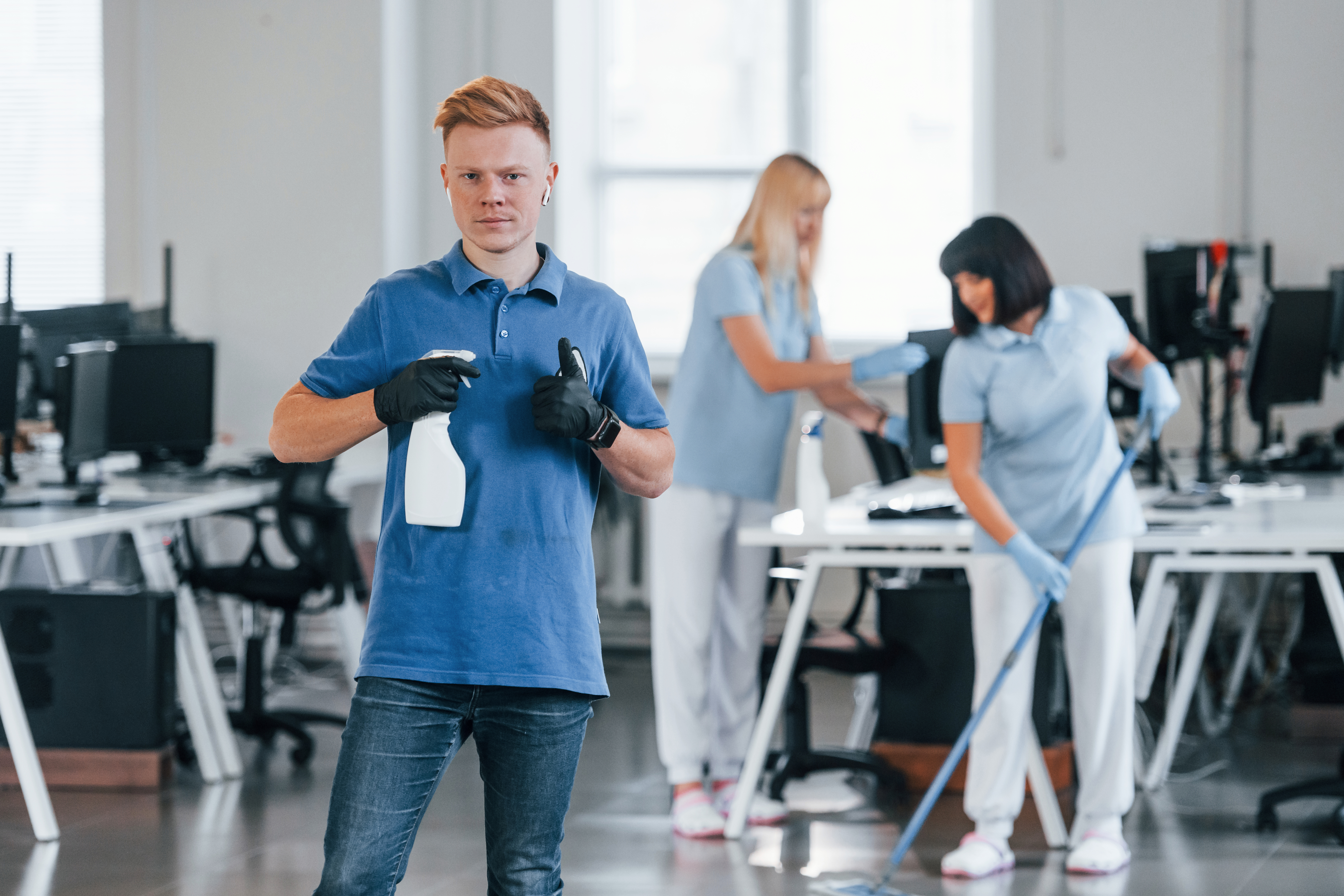 Woman uses vacuum cleaner. Group of workers clean modern office together at daytime