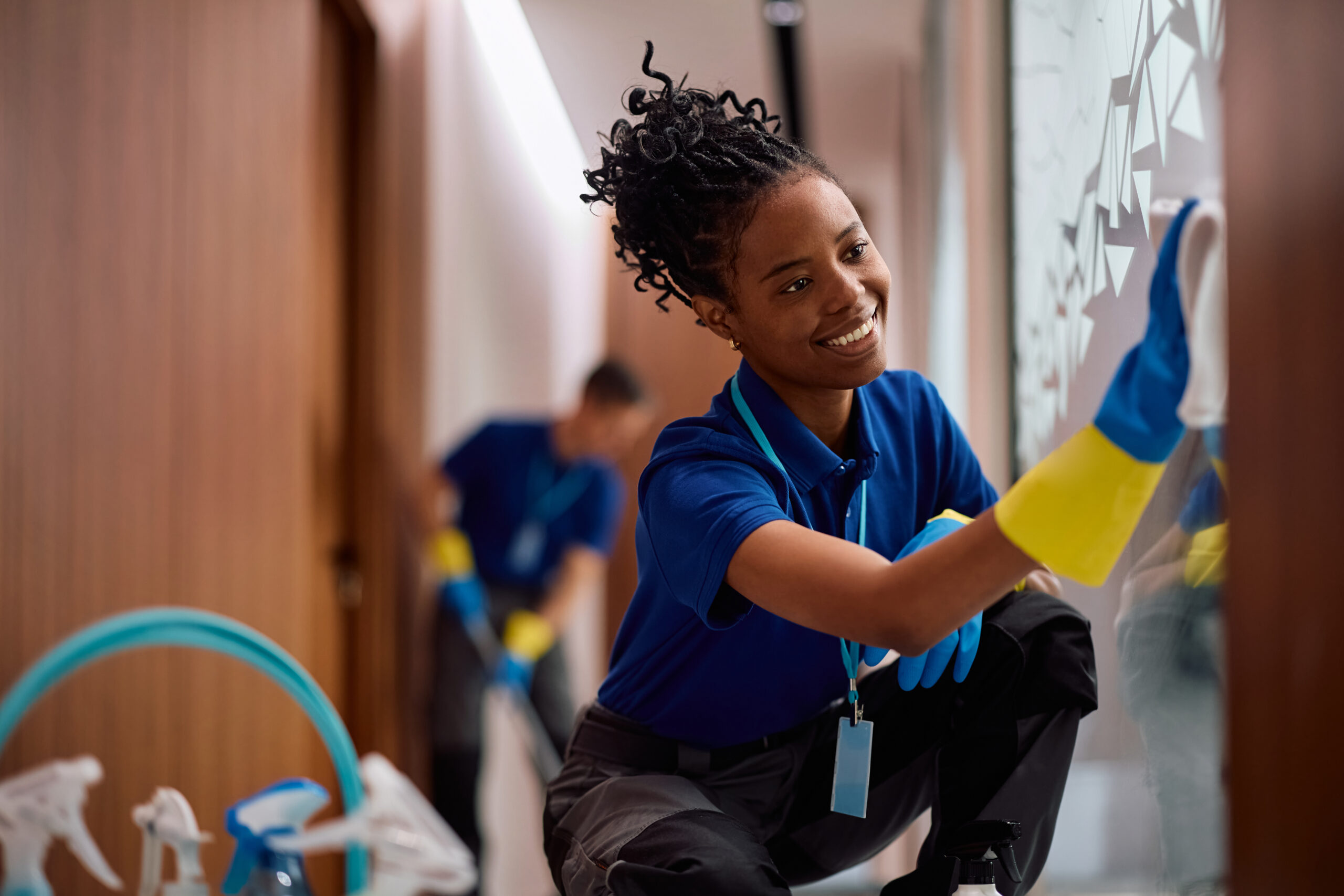 Happy black female cleaner wiping glass walls in an office building.
