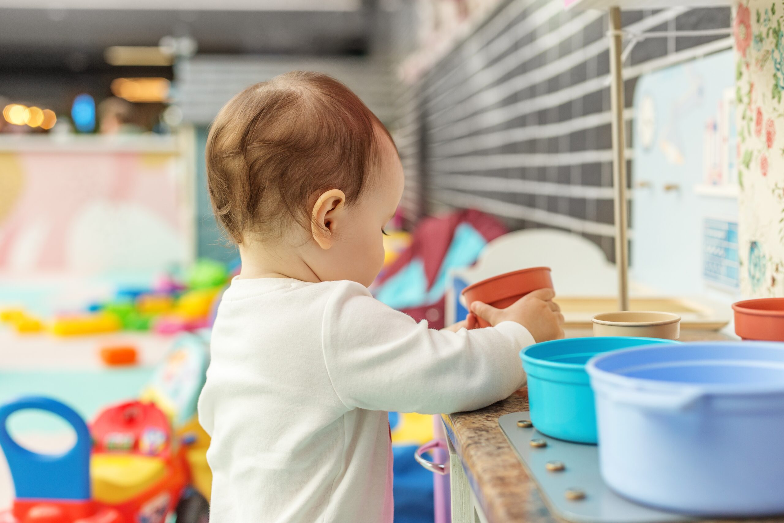 Toddler playing with toy kitchen utensils in daycare playroom. Early years.