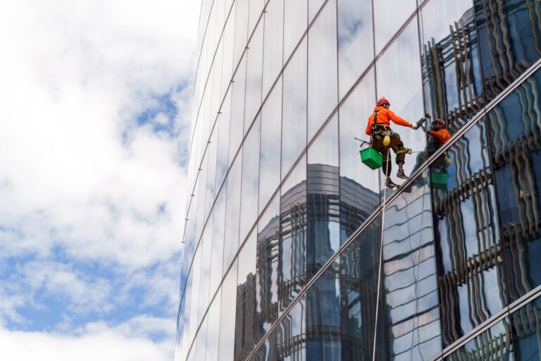 Worker in safety gear clean the windows of a tall glass building